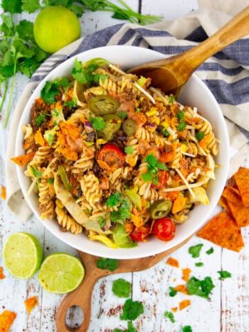 Taco pasta salad in a white bowl with a wooden spoon on a white wooden board