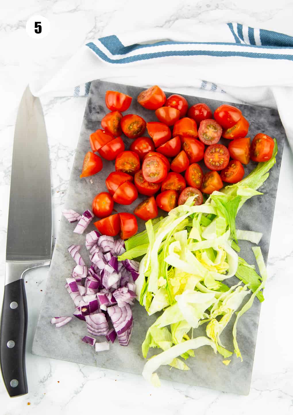 halved cherry tomatoes and chopped lettuce and onion on a cutting board with a large knife 