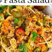 Taco pasta salad in a white bowl with a wooden spoon on a white wooden board with a text overlay