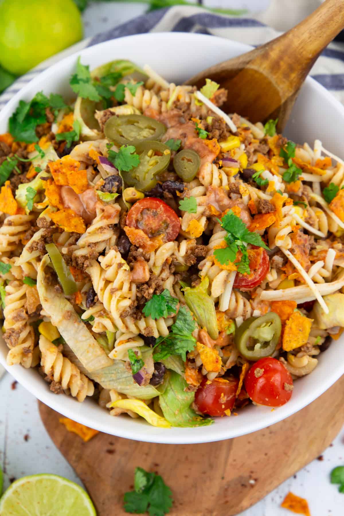 pasta salad in a white bowl with a wooden spoon on a wooden board 