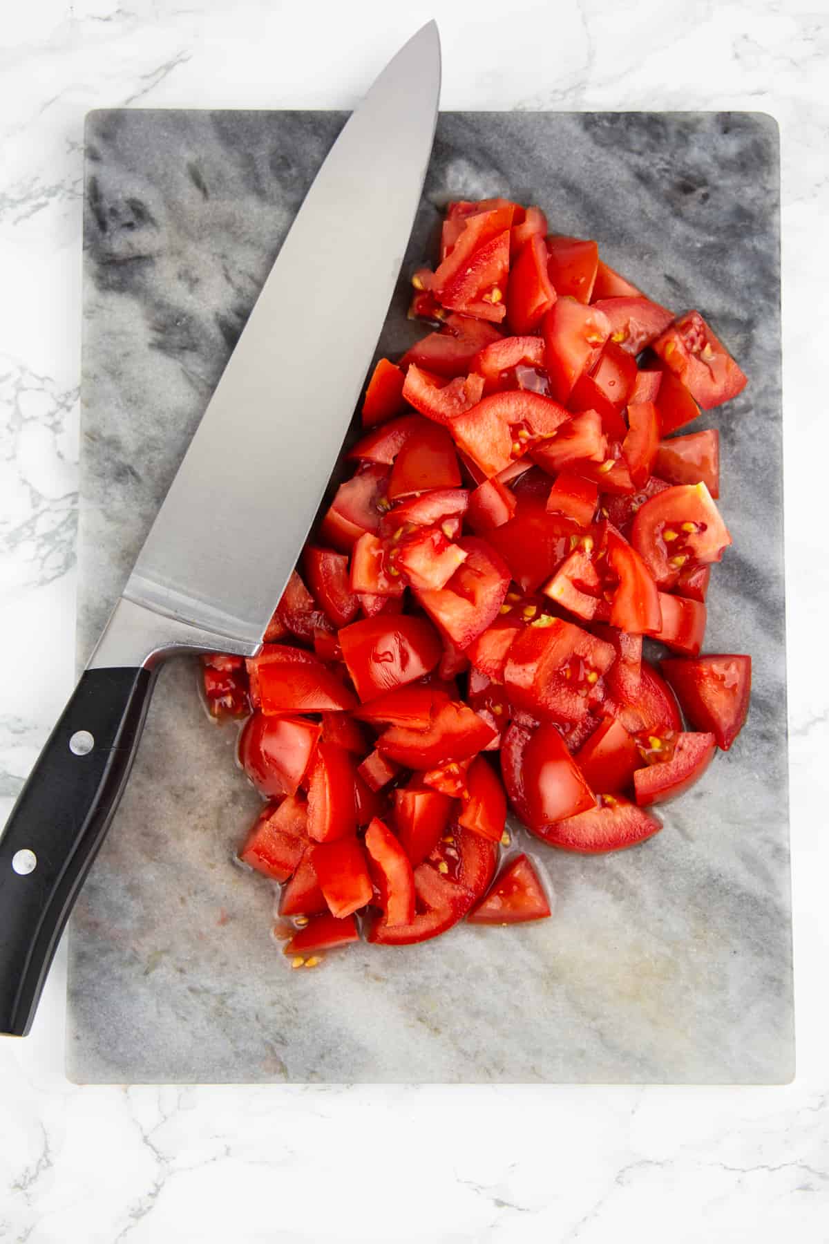 chopped tomatoes on a marble chopping board with a large knife on the side 