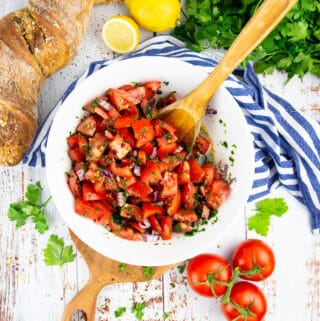 tomato onion salad in a white bowl on a wooden board with parsley in the background