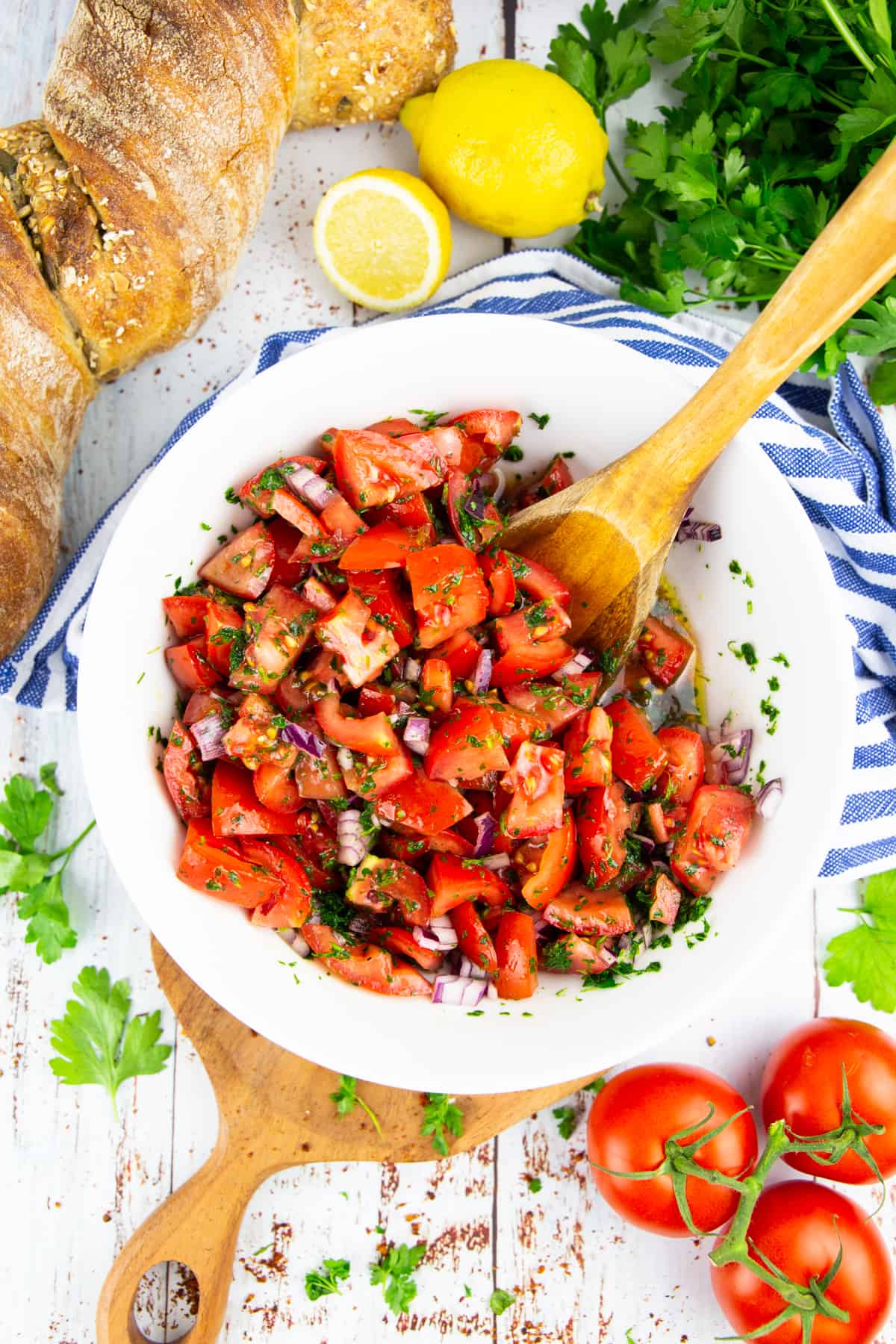 a white bowl with tomato salad with a wooden spoon with a loaf of bread in the background 
