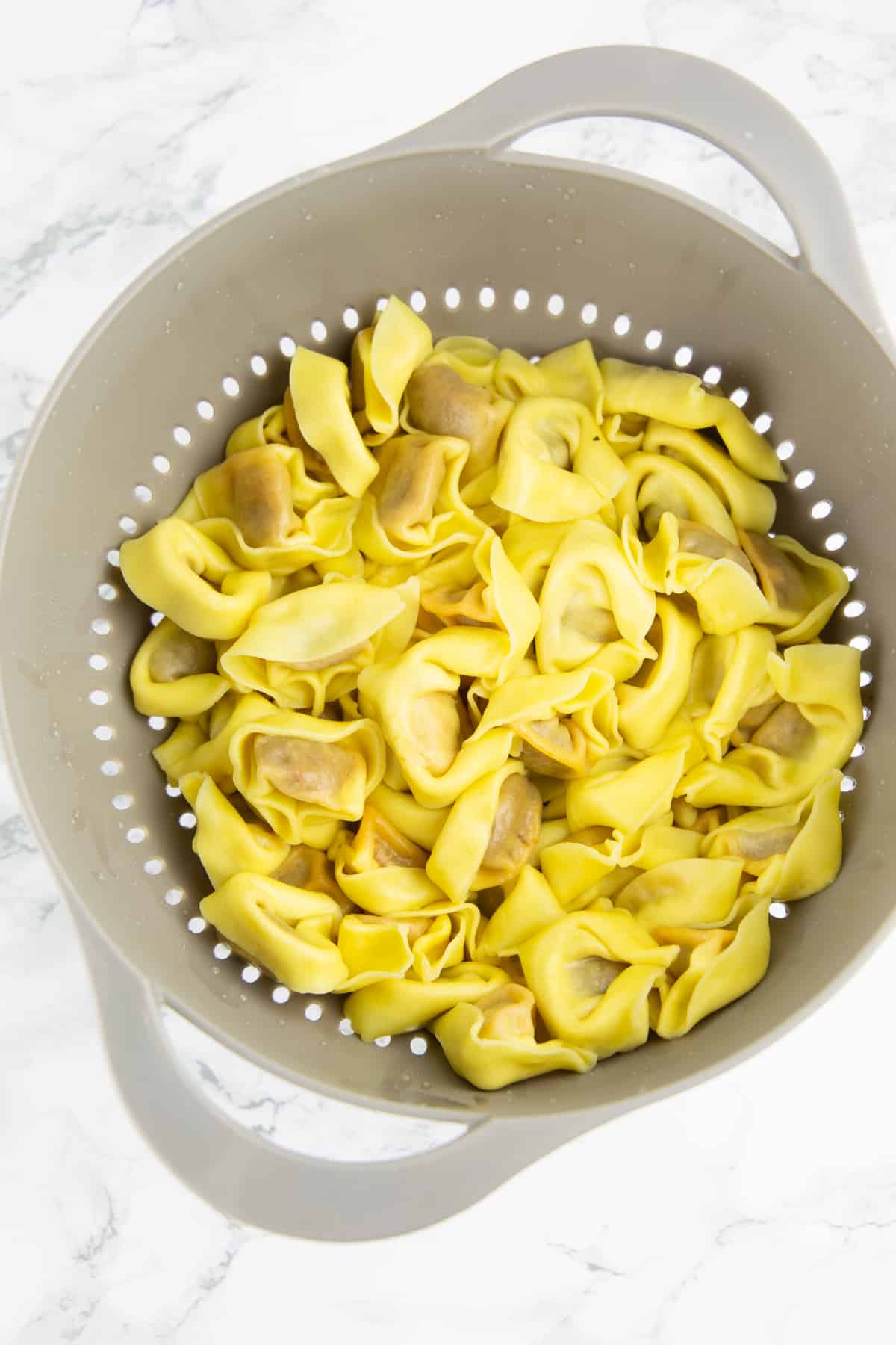 cooked tortellini in a grey colander on a marble countertop 