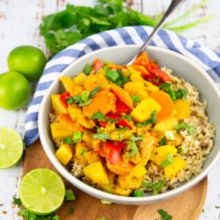 yellow curry with bell pepper and carrots over brown rice in a grey bowl