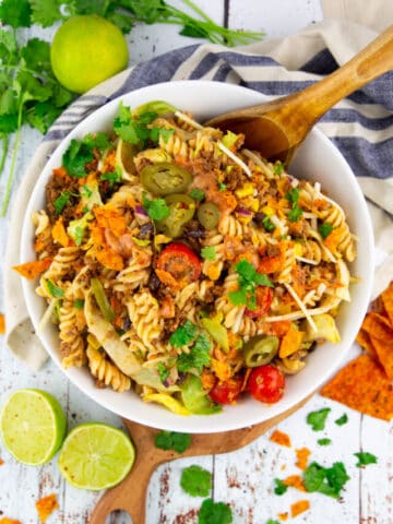 Taco pasta salad in a white bowl with a wooden spoon on a white wooden board