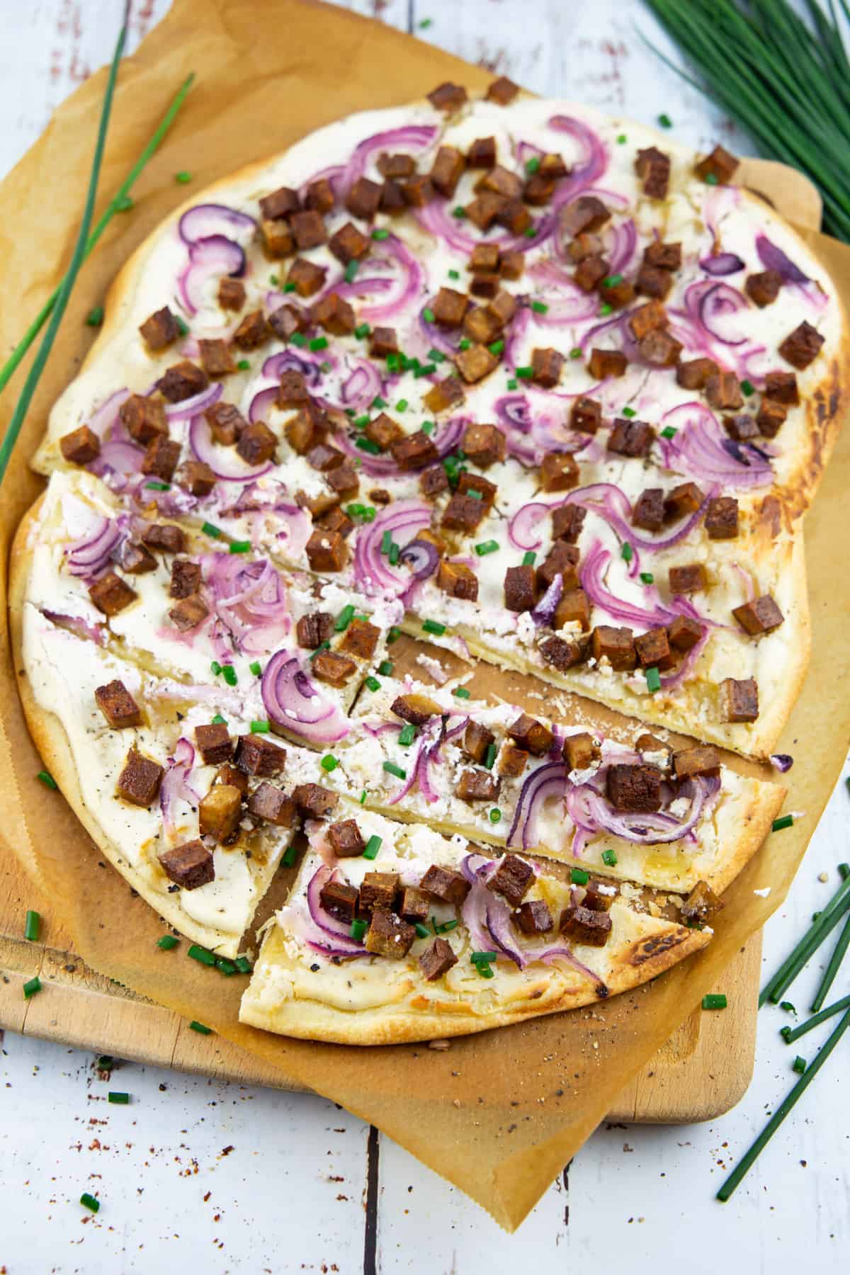 a flammkuchen with smoked tofu and red onions on a cutting board with parchment paper 