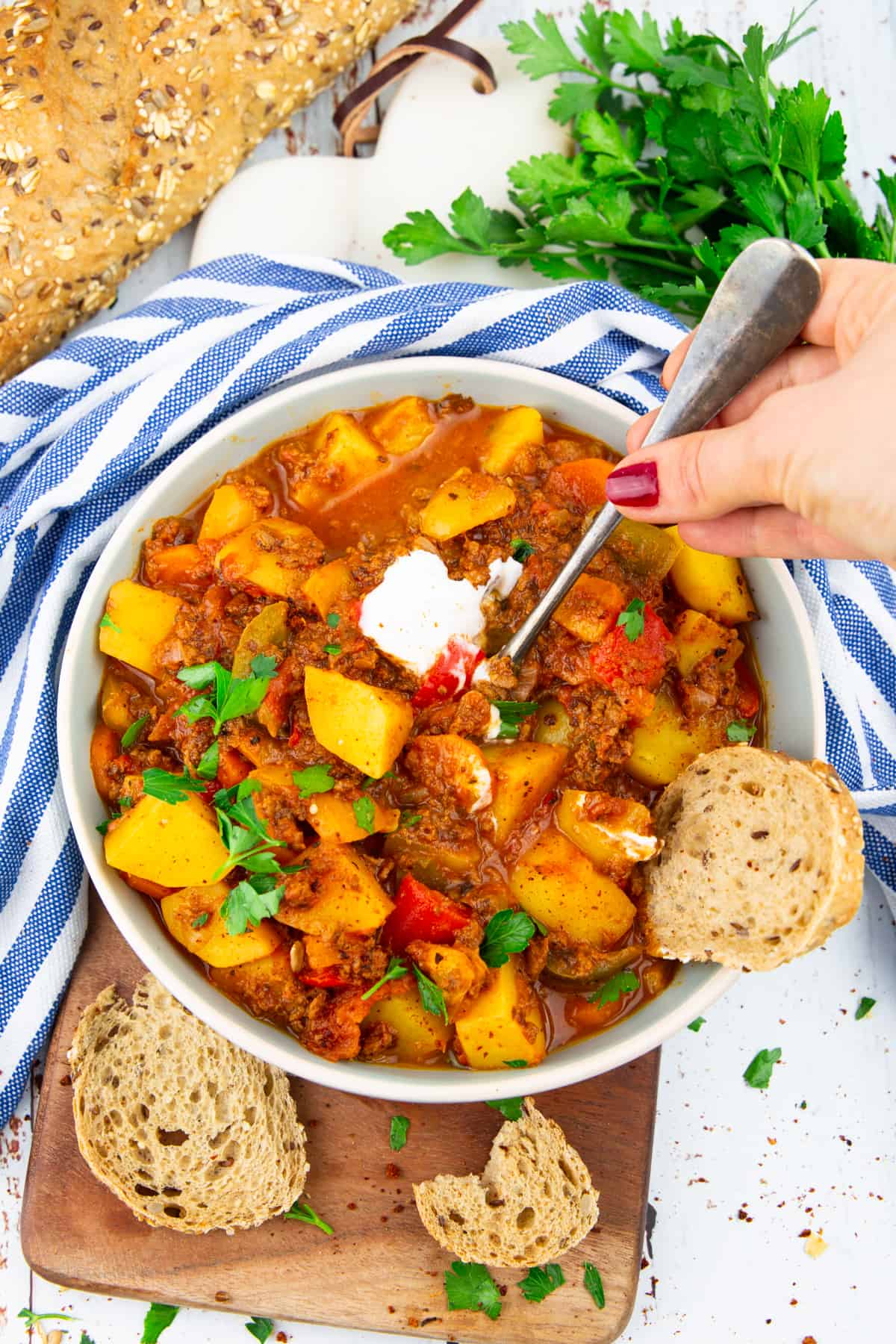 a hand holding a fork in a bowl with potato stew with bell peppers 