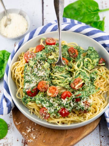 a grey bowl with spinach tomato pasta on a wooden board