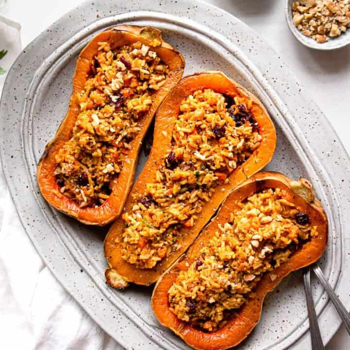 three stuffed butternut squash on a grey plate with cutlery on the side