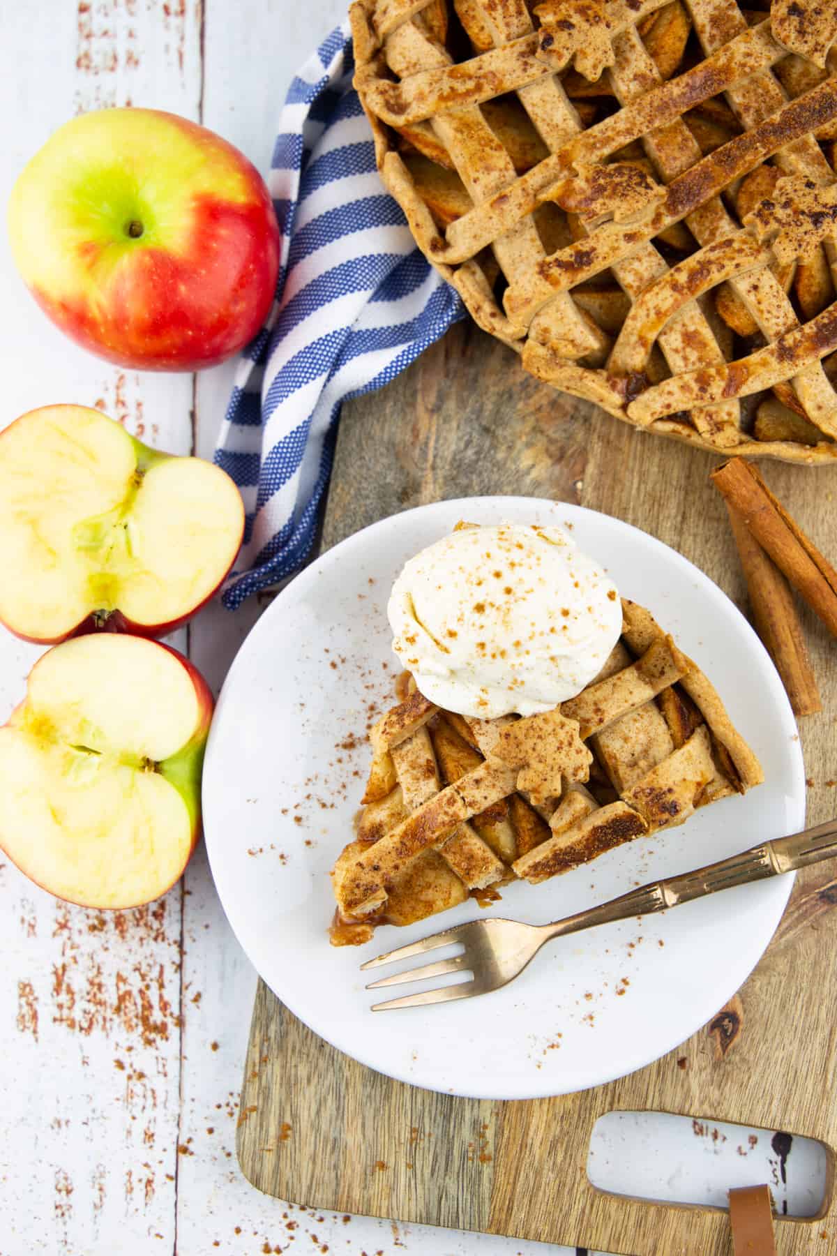 vegan apple pie on a white plate on a wooden board with apples on the side 