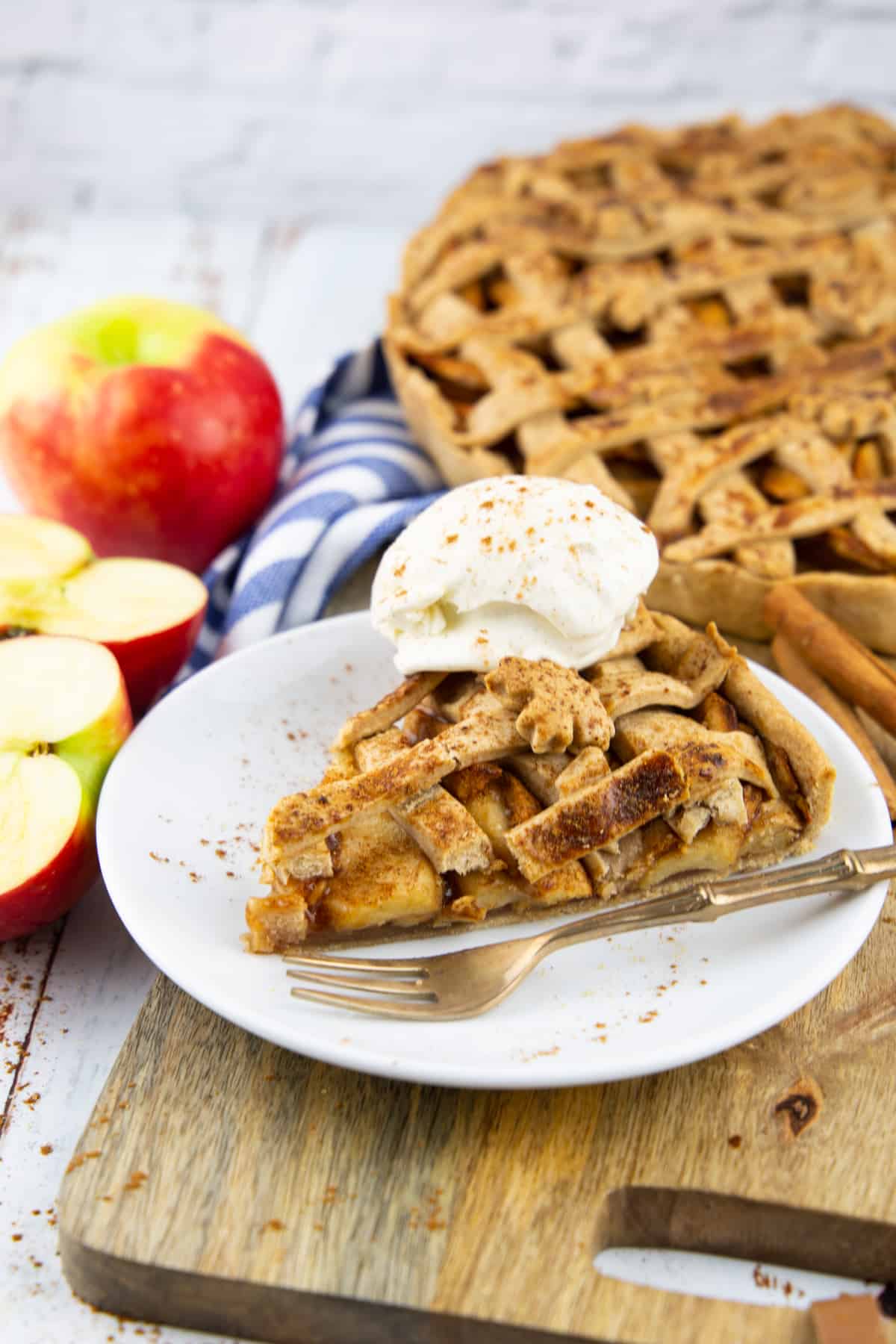 a slice of vegan apple pie on a white plate with the rest of the pie in the background 