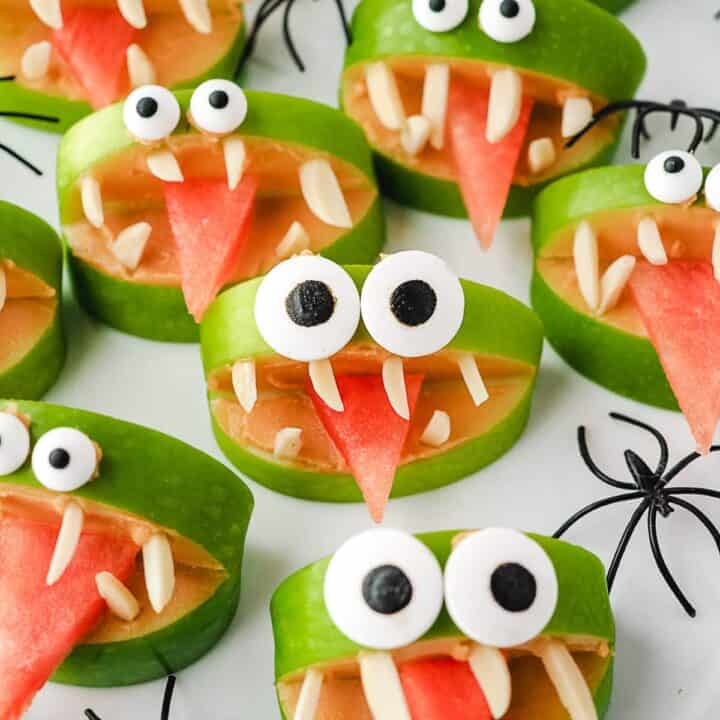apple monsters on a white countertop decorated with plastic spiders