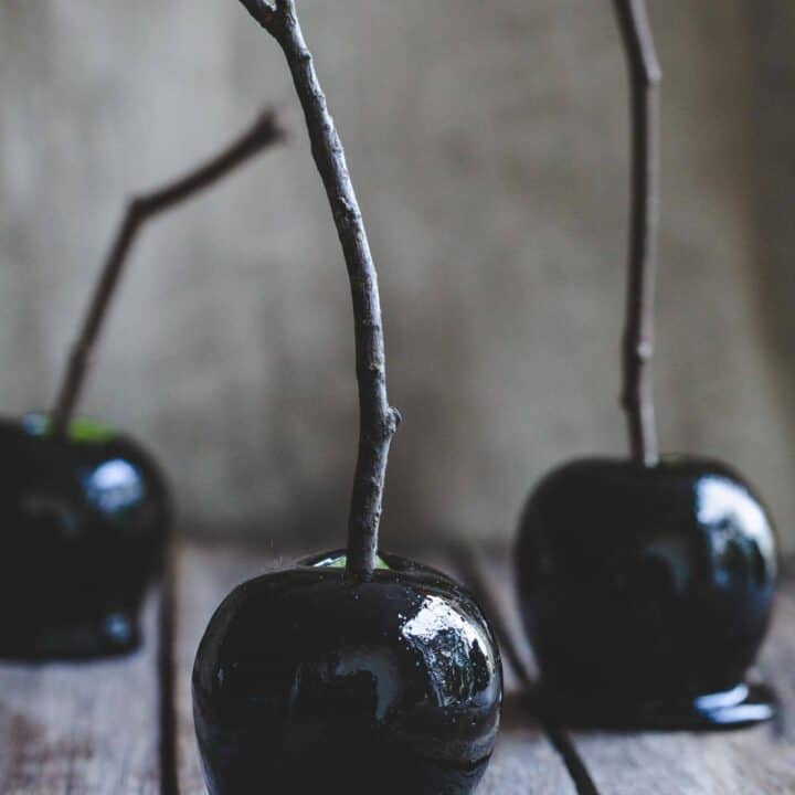 three black candy apples on a wooden board with a grey background