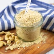 Vegan Parmesan cheese in a glass jar with a white spoon on a wooden board