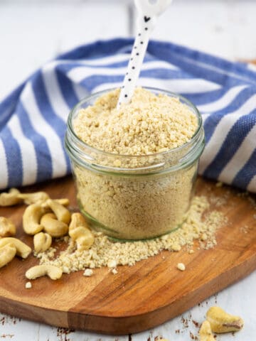 Vegan Parmesan cheese in a glass jar with a white spoon on a wooden board