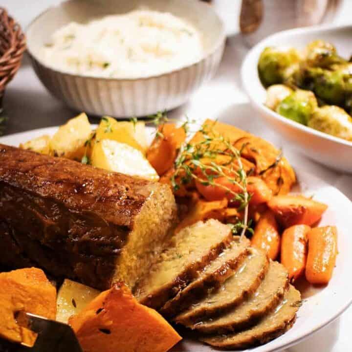 a vegan roast on a plate with carrots, pumpkin, and potatoes