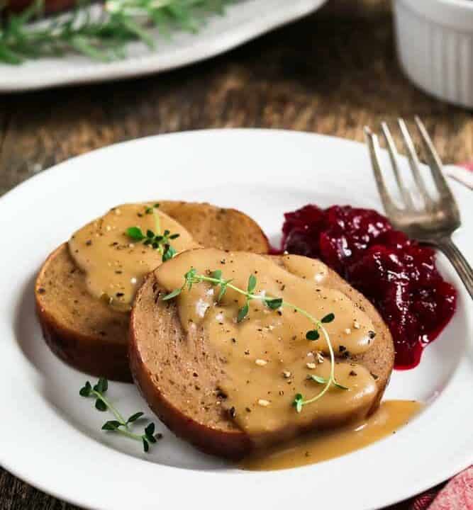 two slices of a vegan roast on a white plate with gravy and cranberry sauce