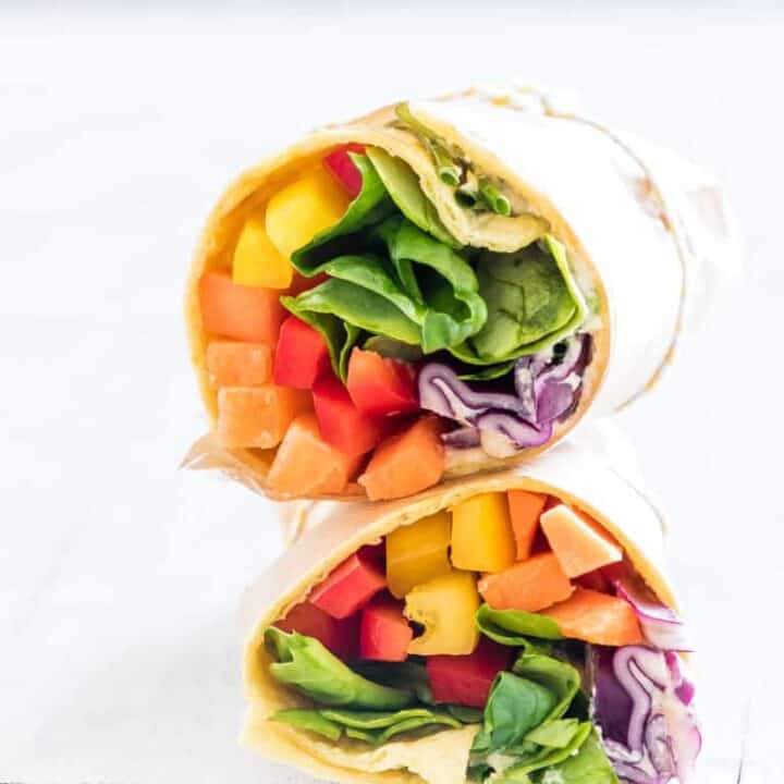 a stack of two vegan wraps filled with vegetables on a white wooden board