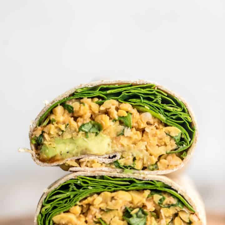a stack of vegan wraps filled with chickpeas and lettuce on a wooden board