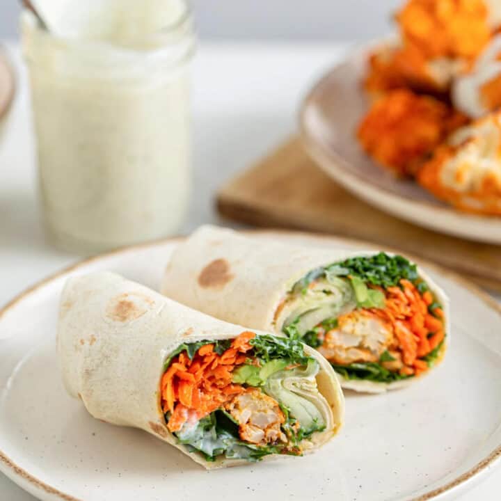two vegan buffalo cauliflower wraps on a white plate with a jar of ranch dressing in the background