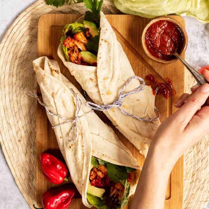 two vegan wraps on a wooden board with a hand holding a spoon with relish