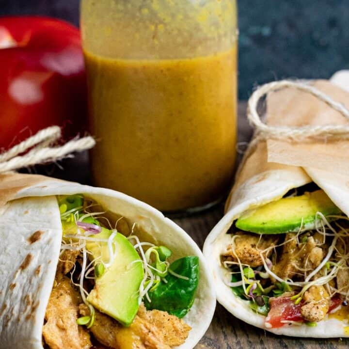 two vegan wraps filled with avocado and vegan chicken on a wooden board with a bottle of honey mustard sauce in the background