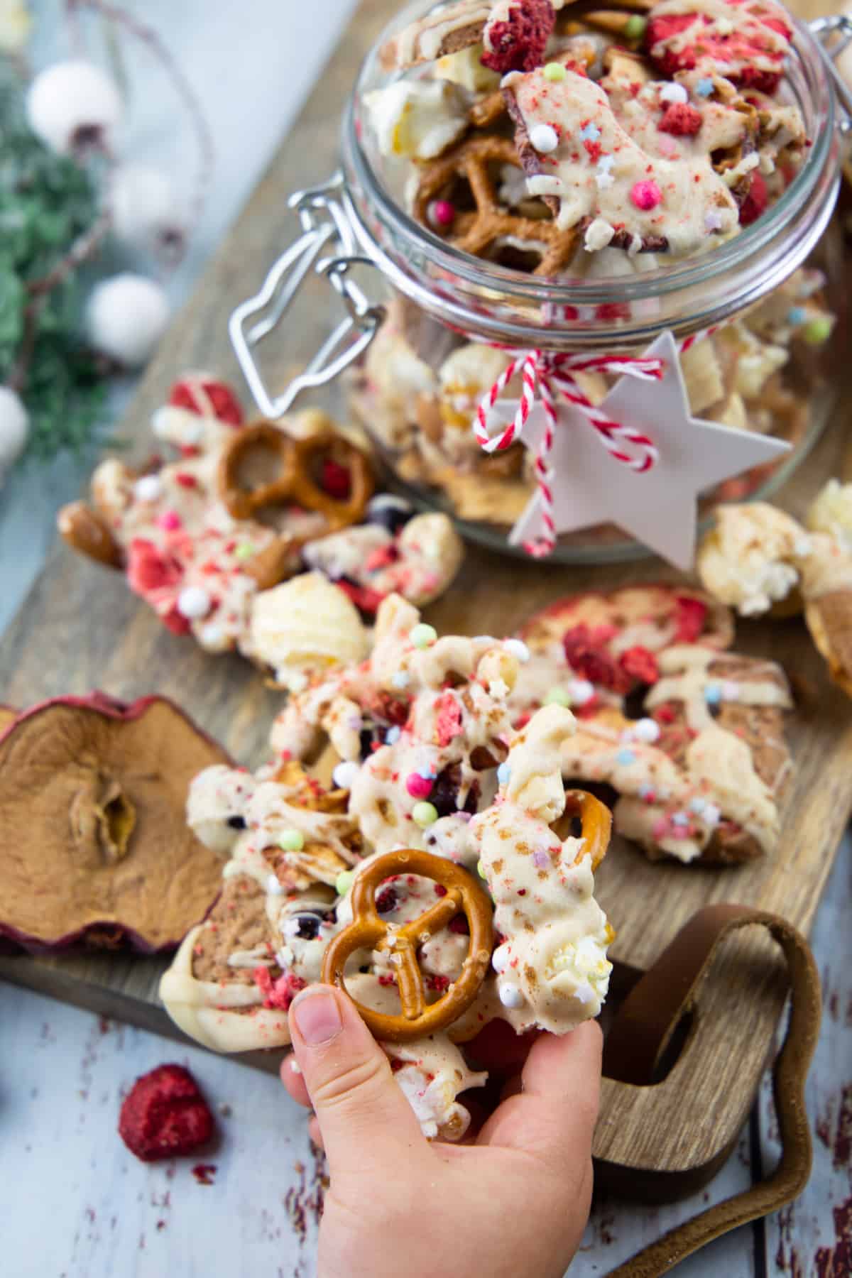 a small hand holding Christmas crunch over a wooden board with a jar in the background 