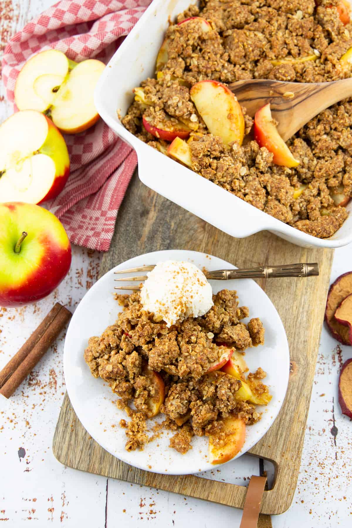 vegan apple crumble in a white casserole dish on a wooden board with a plate on the side 