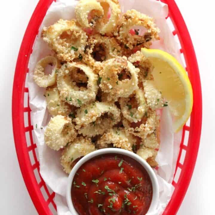 vegan calamari in a small red basket with a small bowl of ketchup and a lemon wedge