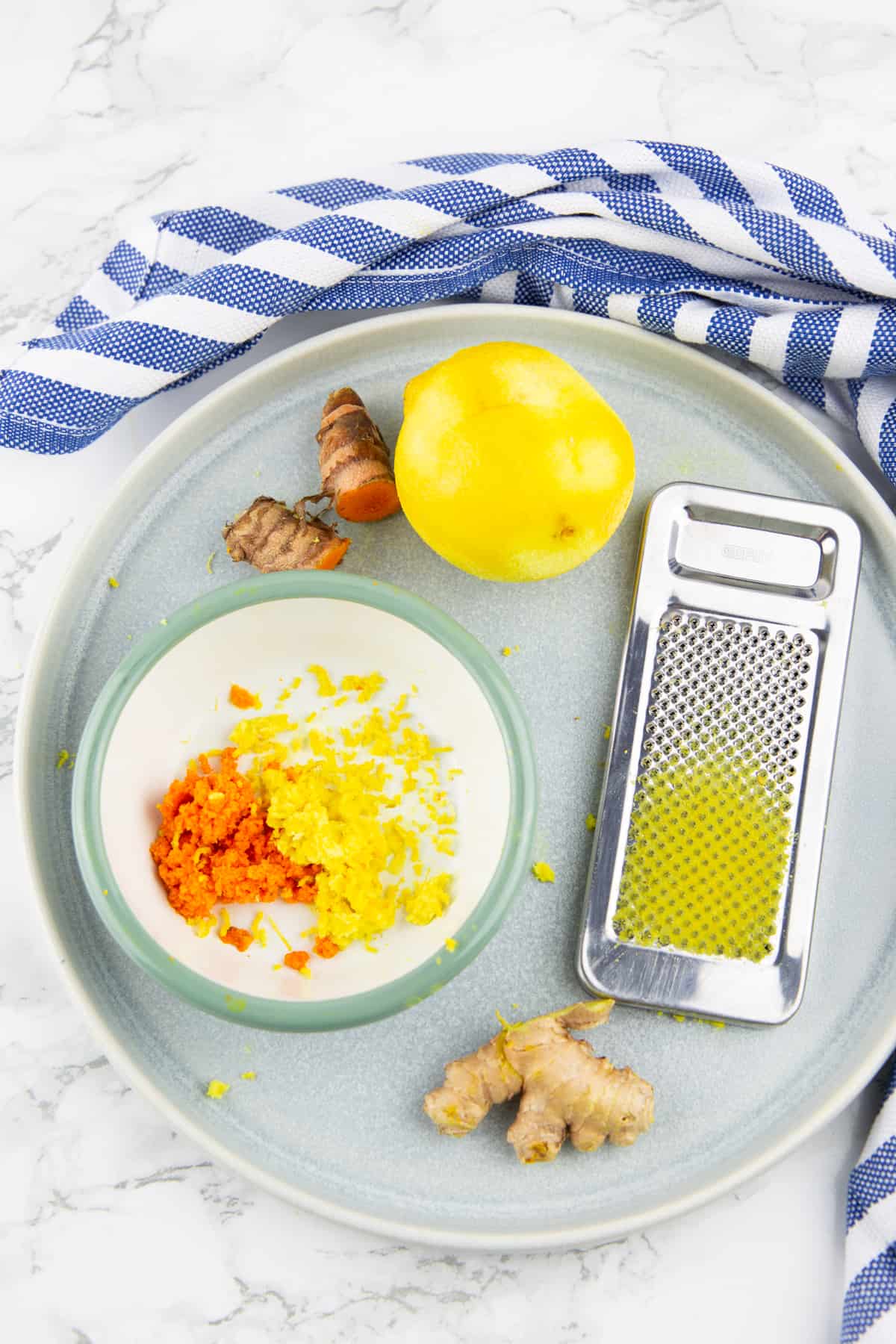 lemon, fresh ginger, and turmeric on a grey plate together with a grater 