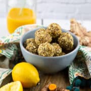 turmeric energy balls in a blue bowl with a glass of smoothie in the background