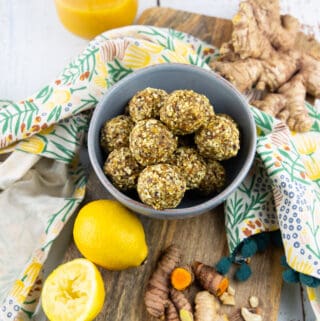 ginger turmeric energy balls in a blue bowl on a wooden board with lemon, ginger, and turmeric on the side