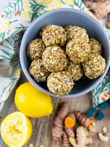 ginger turmeric energy balls in a blue bowl on a wooden board with lemon, ginger, and turmeric on the side