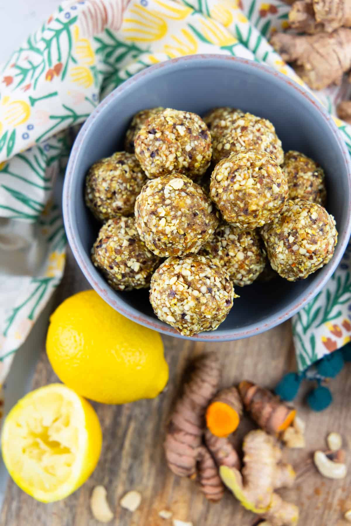 ginger turmeric energy balls in a blue bowl on a wooden board with lemon, ginger, and turmeric on the side 