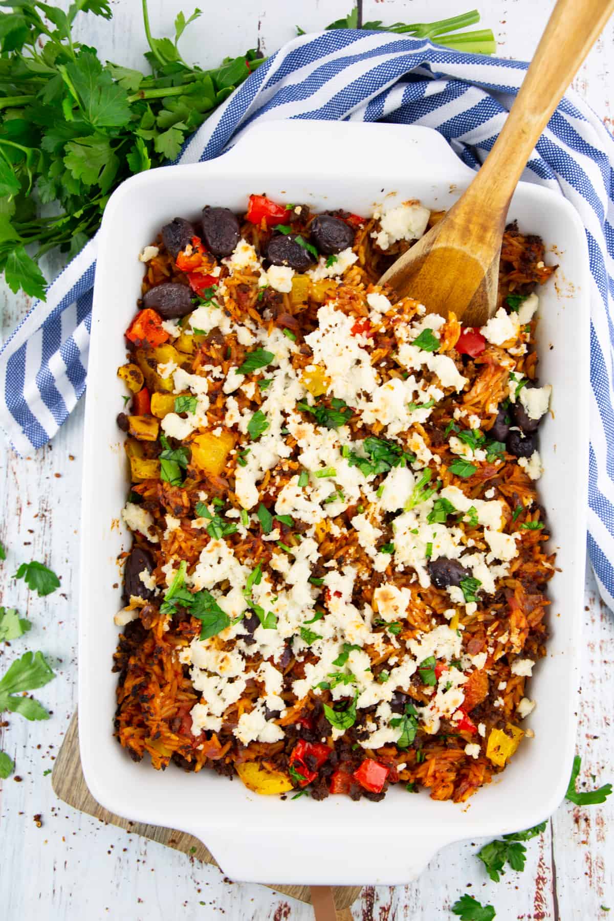 vegan Greek orzo bake in a white casserole dish with a wooden spoon 