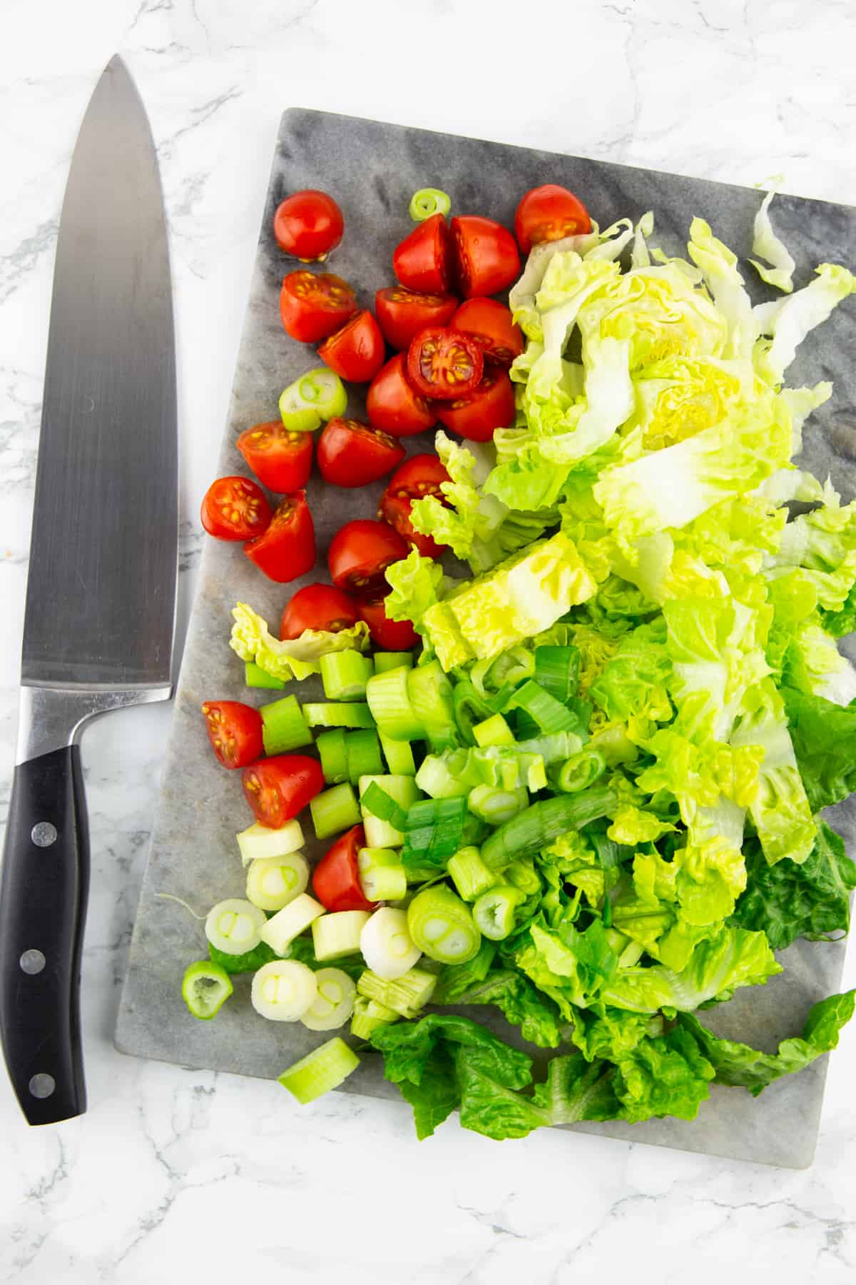 chopped lettuce and tomatoes on a marble chopping board with a large knife on the side 