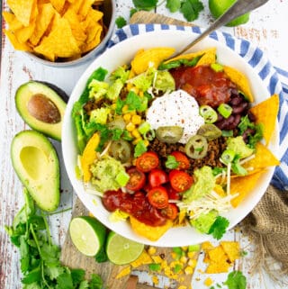 a vegan taco salad in a white bowl on a wooden board with avocado halves on the side