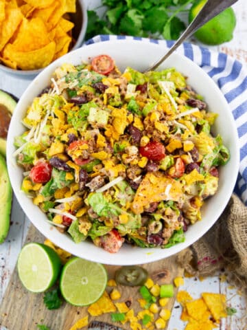 a vegan taco salad in a white bowl with a spoon with limes on the side