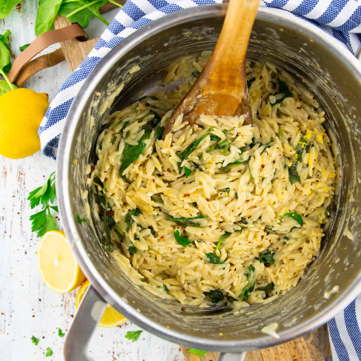 a pot with lemon orzo with spinach on a white wooden board