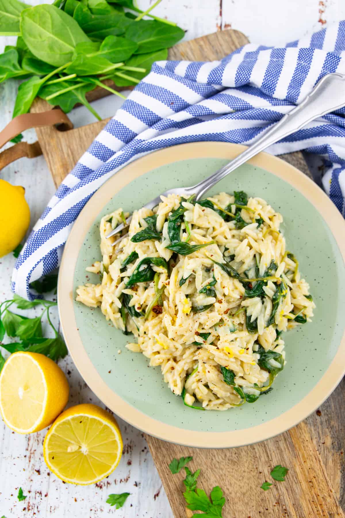 lemon orzo with spinach on a green plate with a fork on a wooden board 