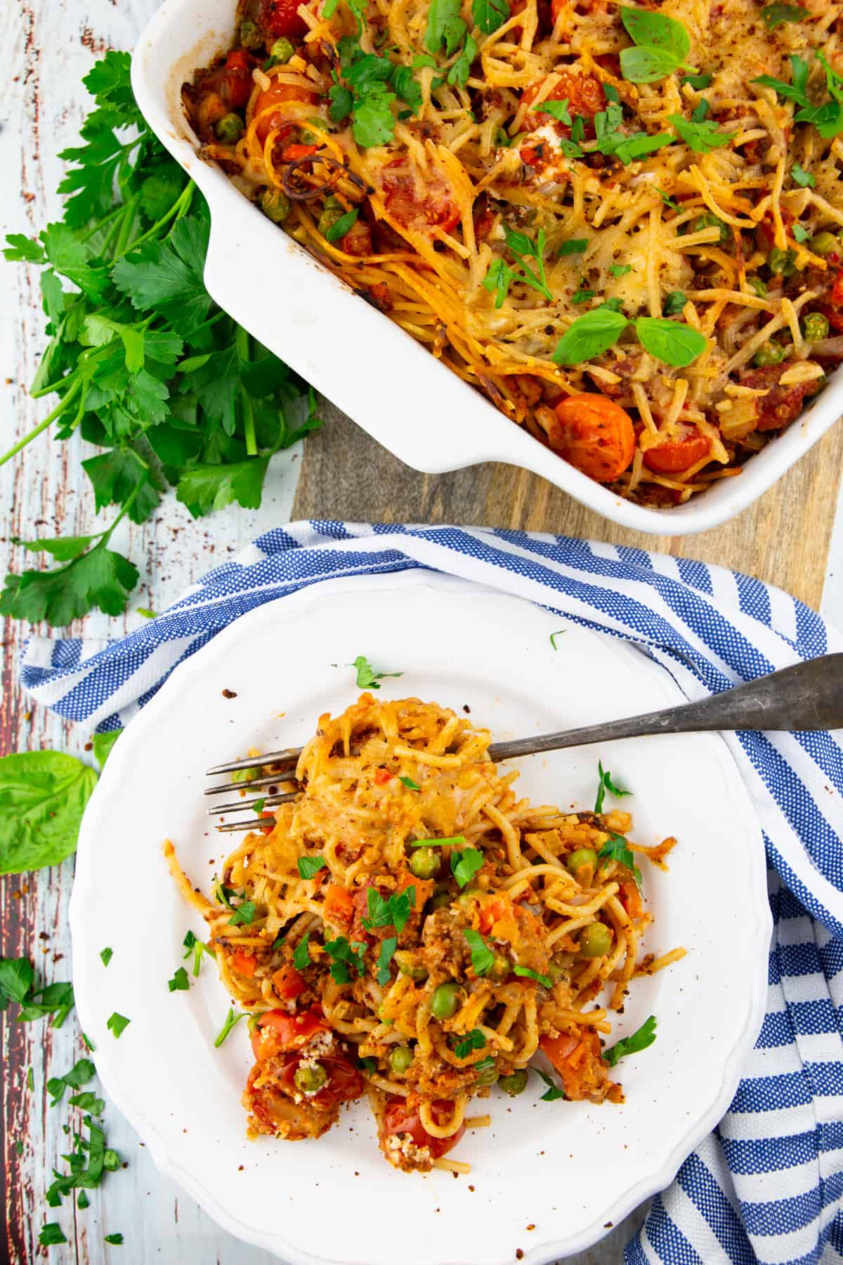Spaghetti with bolognese sauce and peas on a white plate with a casserole dish in the background 