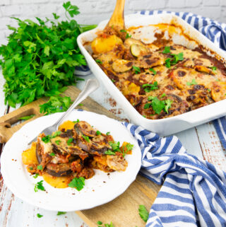 vegan moussaka on a white plate with a white casserole dish on the side