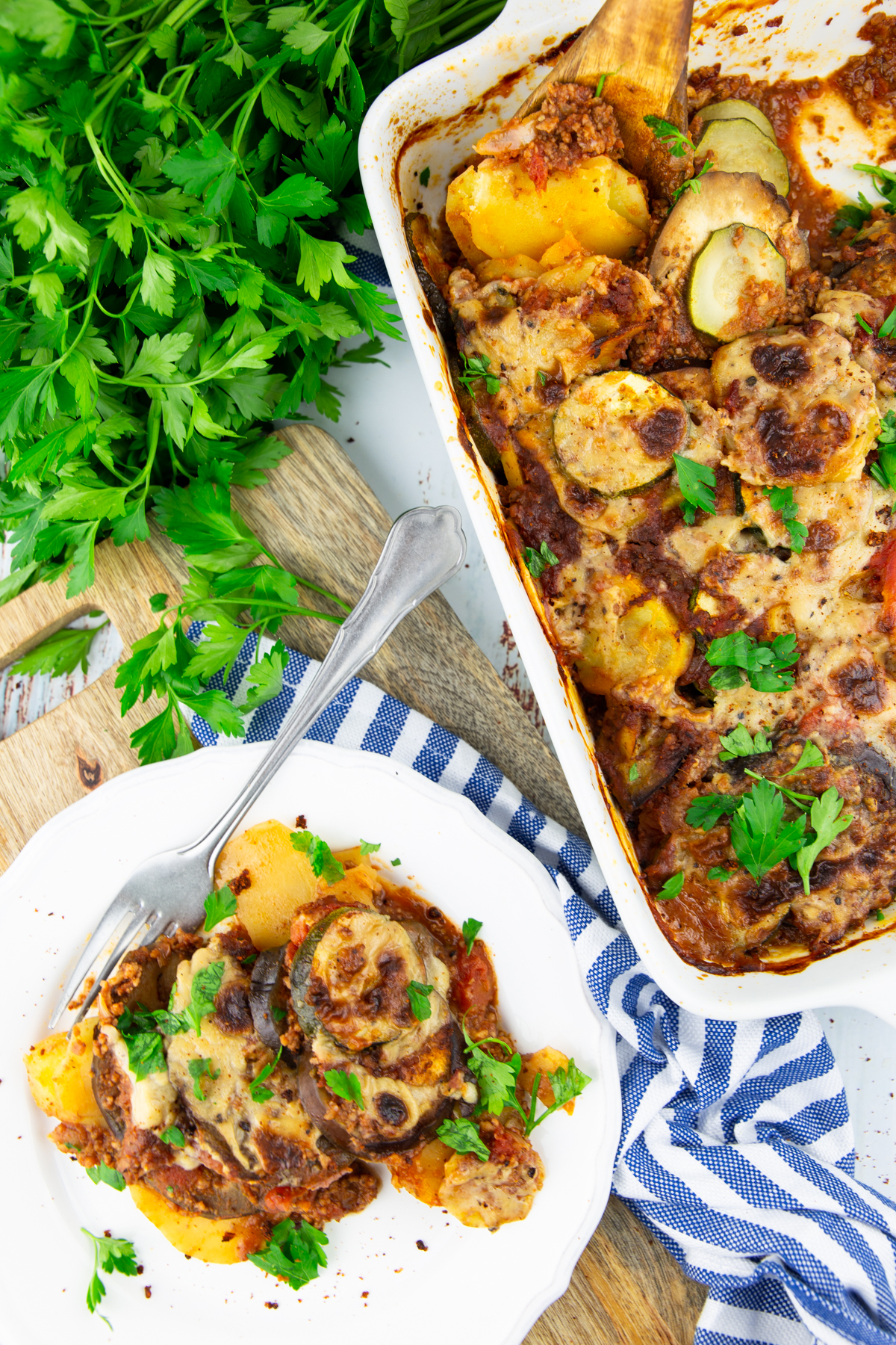 vegan moussaka on a white plate with a white casserole dish on the side 