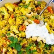 a pan with vegetable biryani topped with a bit of yogurt with herbs