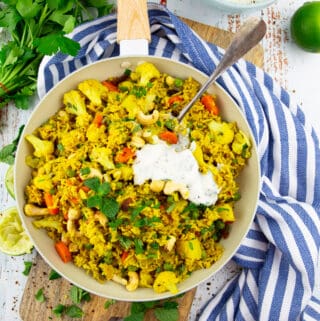 vegetable biryani in a white pan on a wooden board with parsley and mint in the background