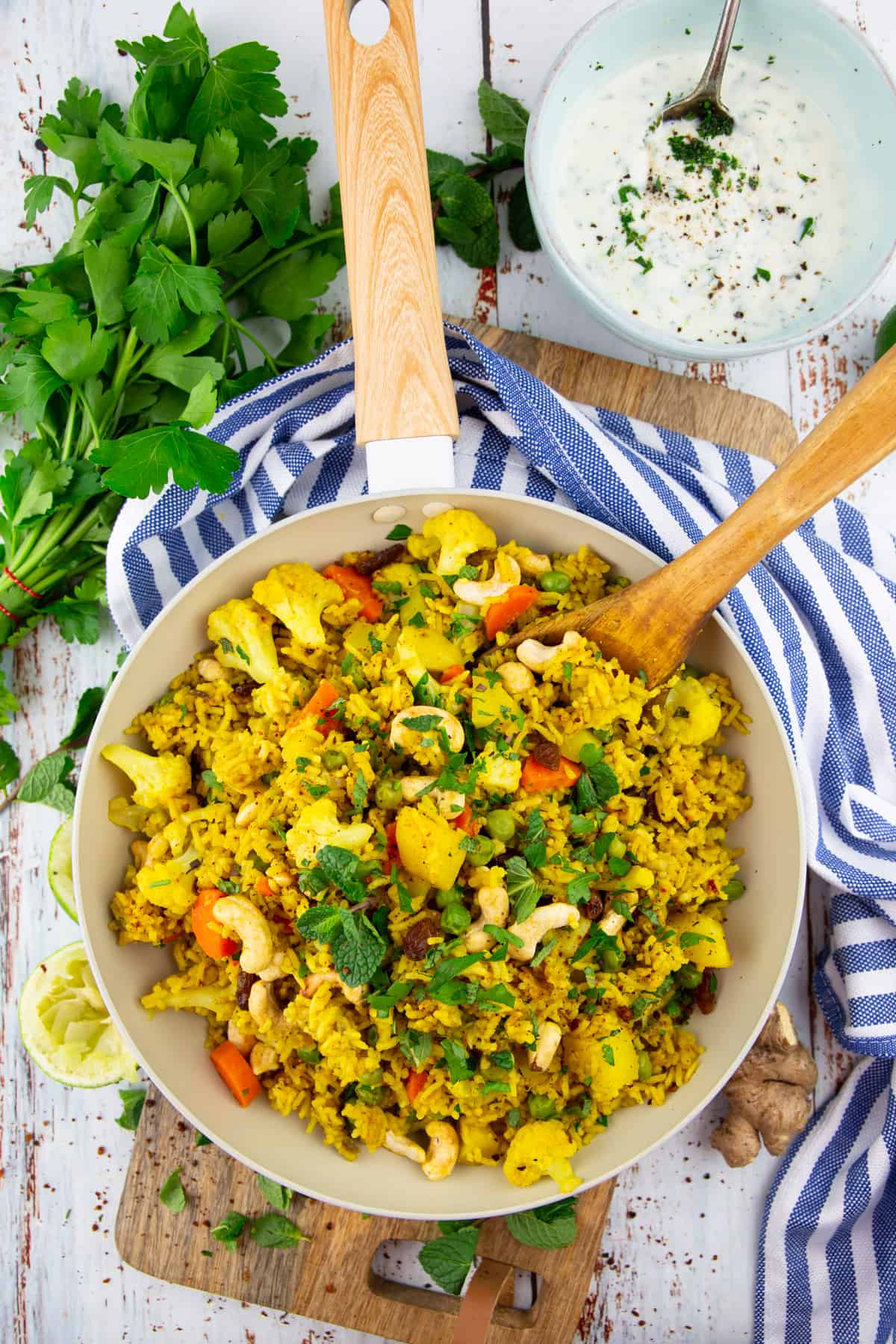 vegetable biryani in a pan with a wooden spoon on a wooden board 