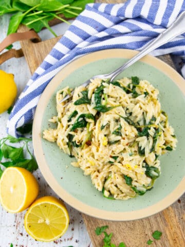 lemon orzo with spinach on a green plate with a fork on a wooden board