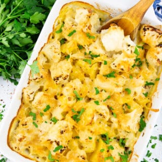 a cauliflower casserole in a white dish with a wooden spoon on a wooden board