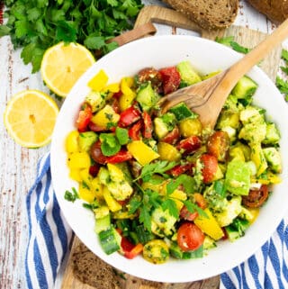 a white bowl with avocado salad with cucumber and cherry tomatoes on a wooden board
